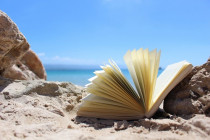 photo d'un livre sur la plage, avec la mer et le ciel bleu en arrière plan
