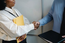 une femme noire portant une enveloppe jaune serre la main à un homme blanc
